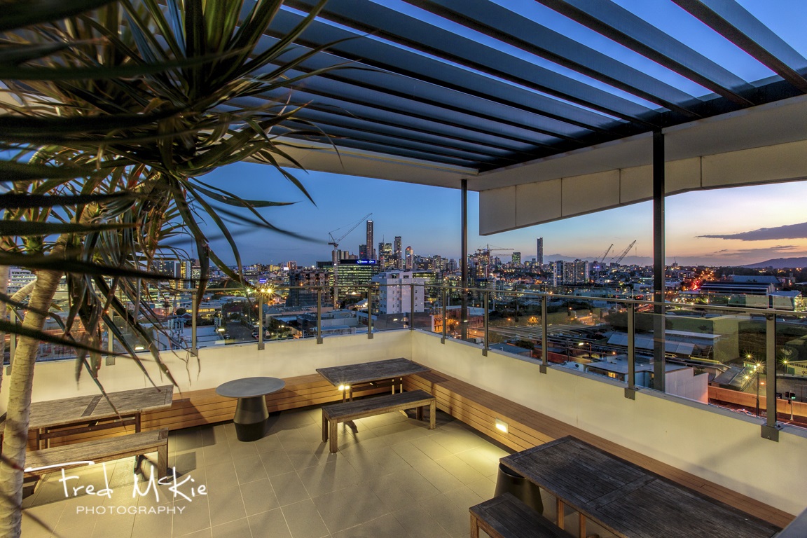 Apartment hotel amenities marketing photography for Code Apartments in Bowen Hills, Brisbane, Queensland, Australia, featuring the sky deck with views to Brisbane CBD at dusk.