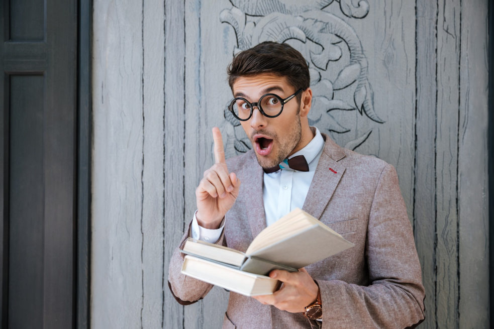 Inspired funny young man in round glasses reading book and having an idea