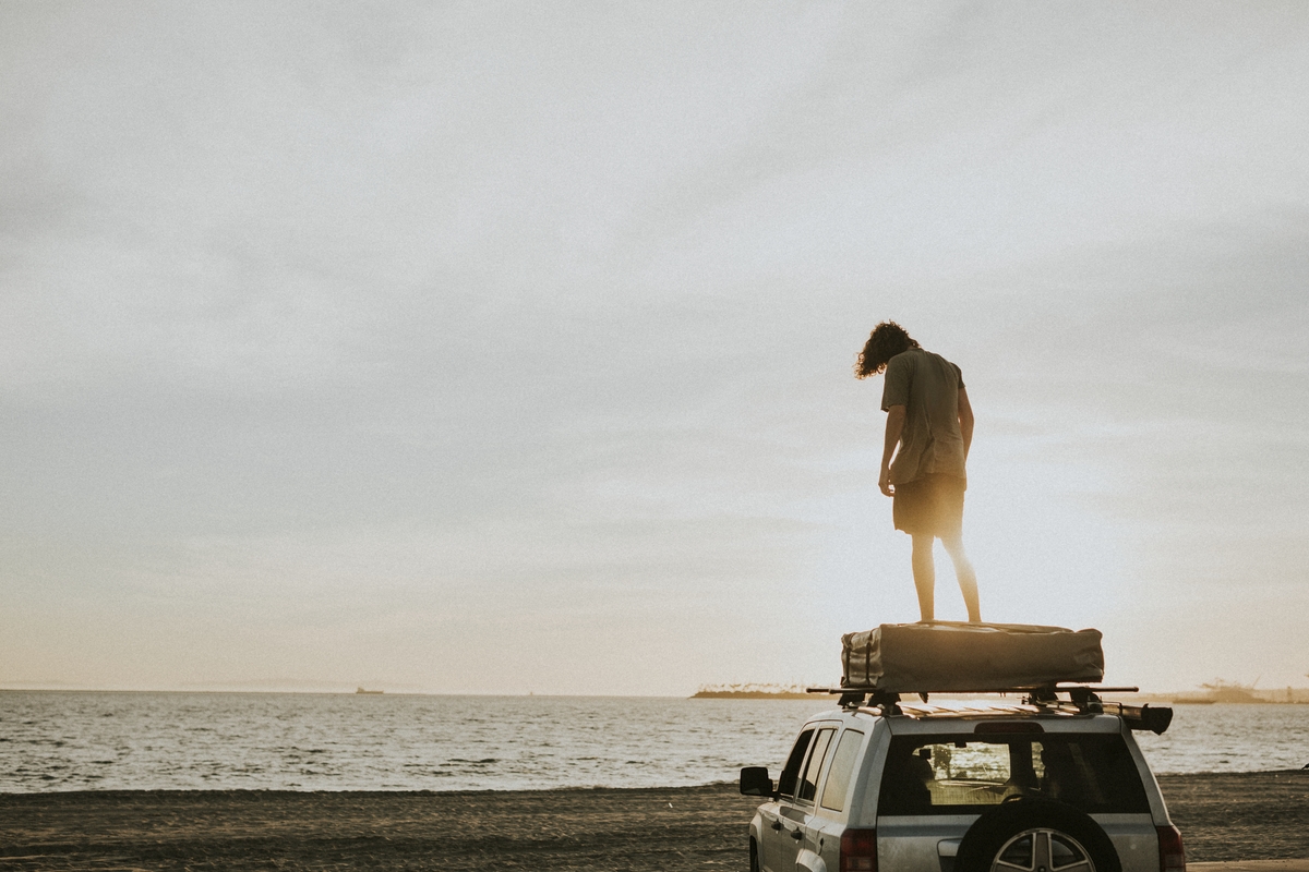 Man standing on a car top at the beach in California, USA